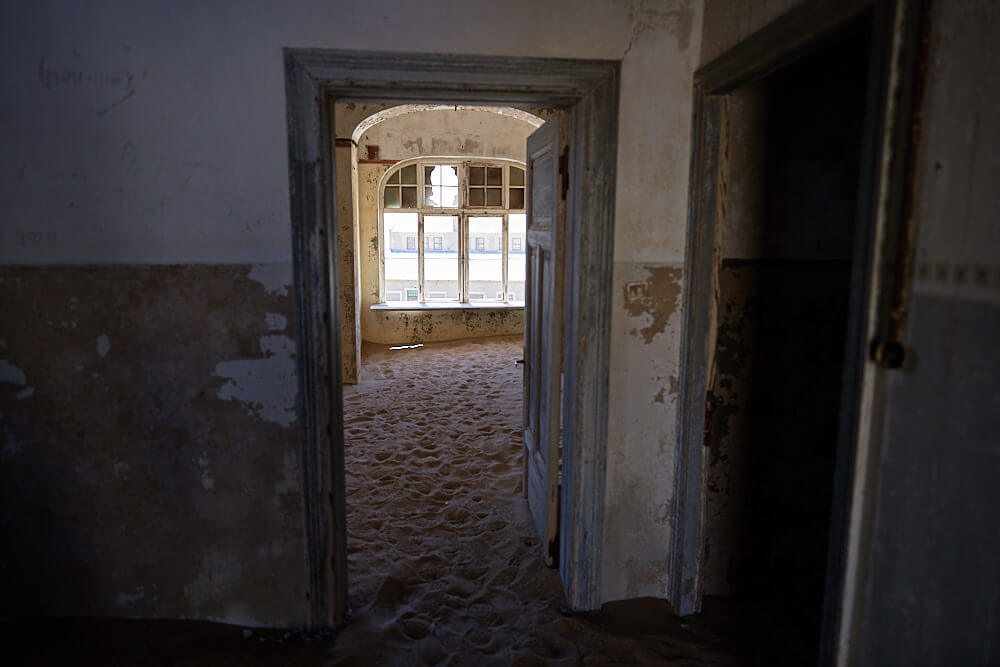 The picture shows the view out of a crumbling house in Kolmanskop.