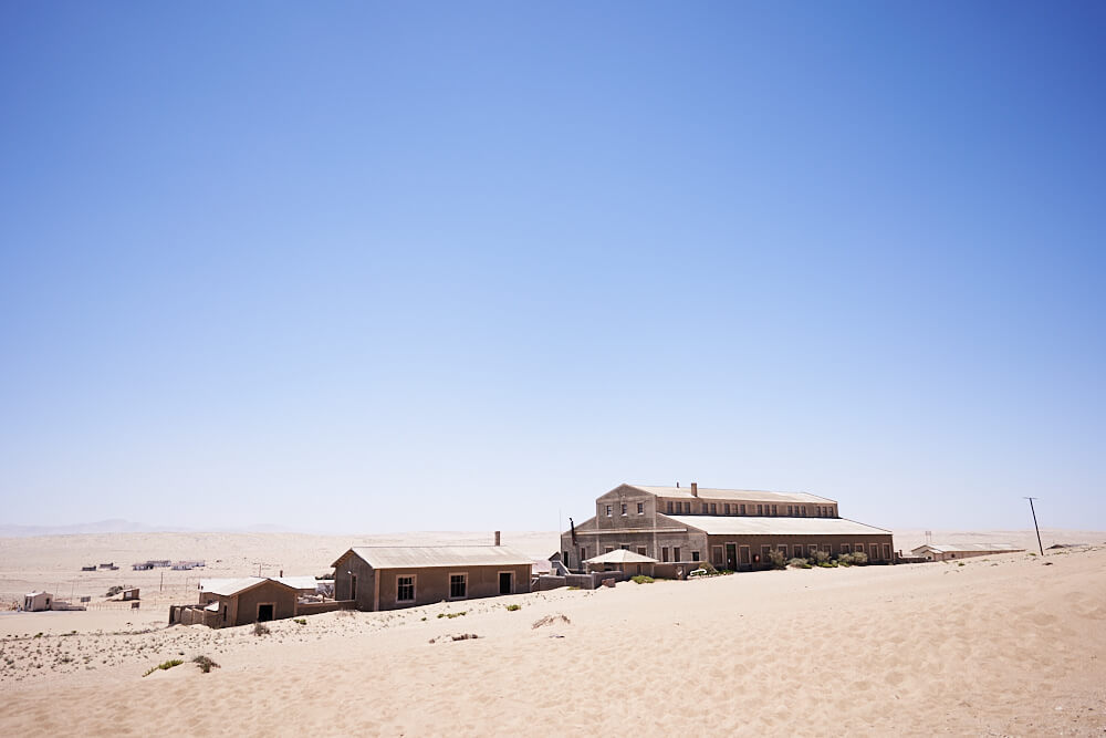 The picture shows parts of Kolmanskop around the desert as a wide-angle shot.