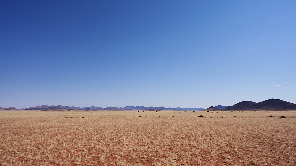 Das Bild zeigt eine Halbwüsten-Landschaft mit verschiedenen Farben vor einer Weite im Namtib Biosphere Reserve.