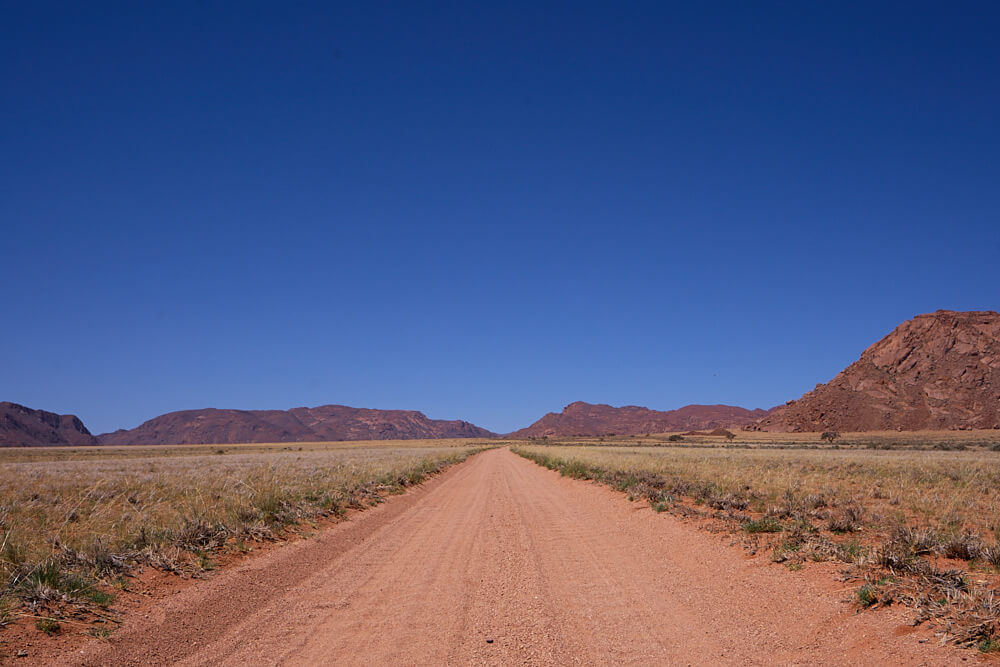 The picture shows a colorful landscape with a gravel road and mountains in the background.