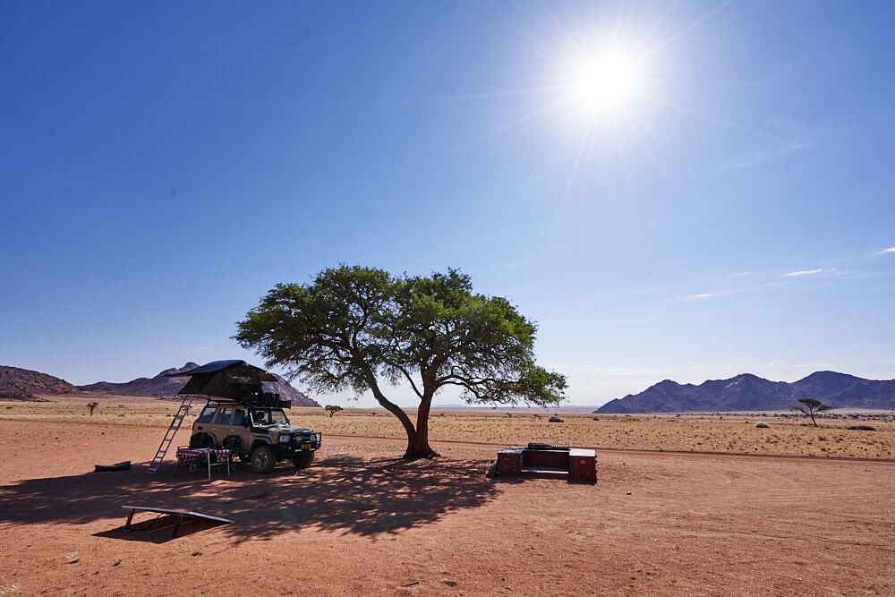 Das Bild zeigt unsere Campsite mit einem schattenspendenden Baum vor einer unendlichen Weite im Namtib Biosphere Reserve.
