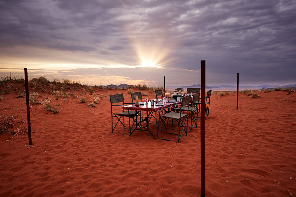Dieses Bild zeigt die morgendliche Wüstenstimmung am Frühstückstisch mit durch die dunklen Wolken brechender Sonne