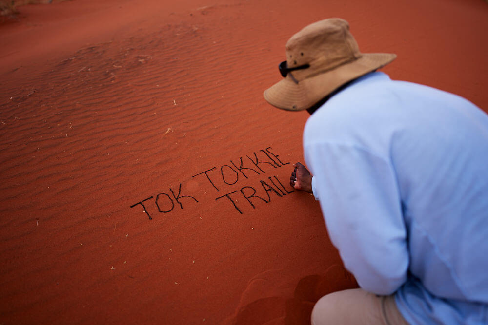 Unser Guide schreibt mit den dunklen Partikeln das Wort 'Tok Tokkie Trails' in den Sand.