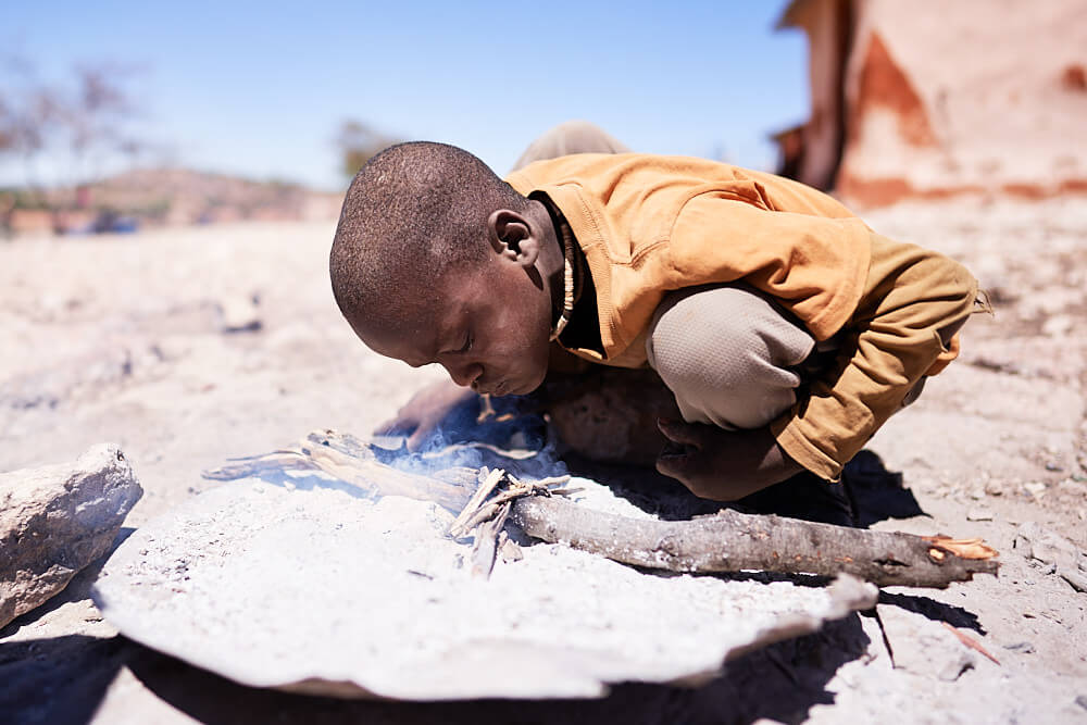 Das Bild zeigt einen jungen Himba beim Feuer entfachen