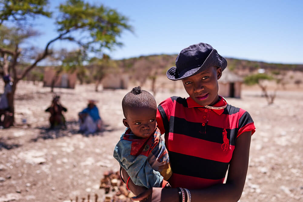 Das Bild zeigt ein Portrait einer modernen Himba mit ihrem Baby.