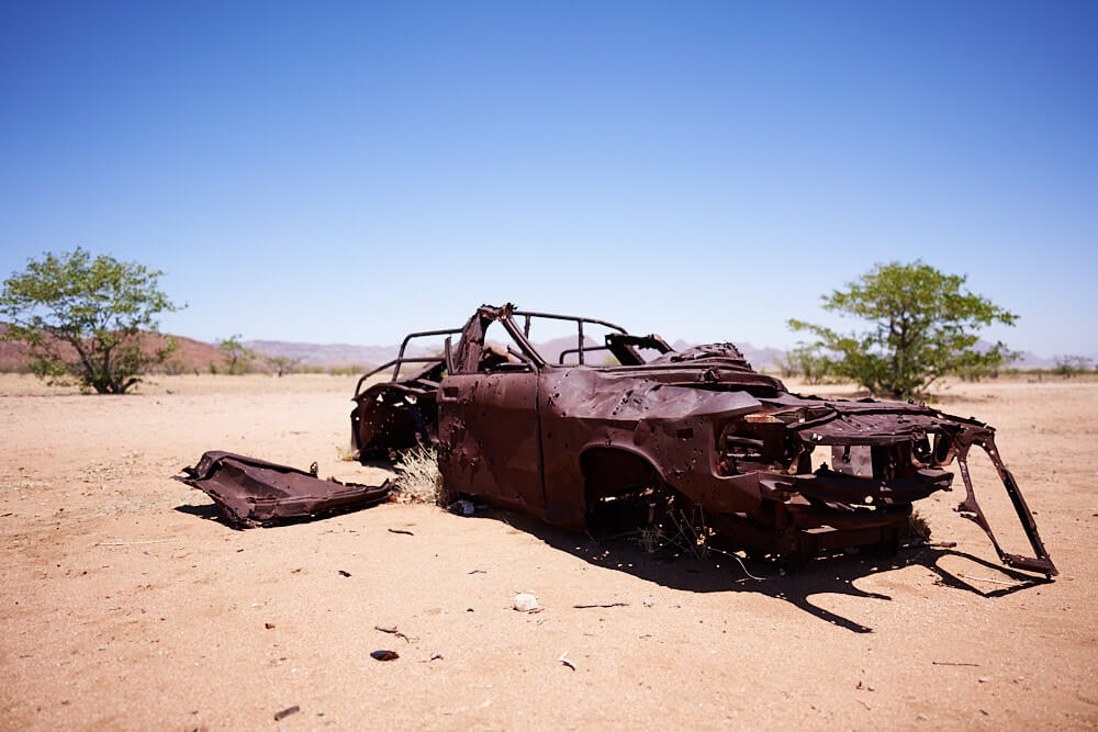 The picture shows the rusted and shattered wreckage of a passenger car.