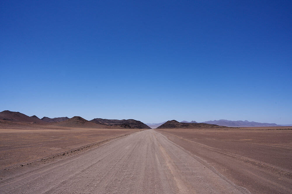 The picture shows a gravel road in the middle of the Kaokoland wasteland.