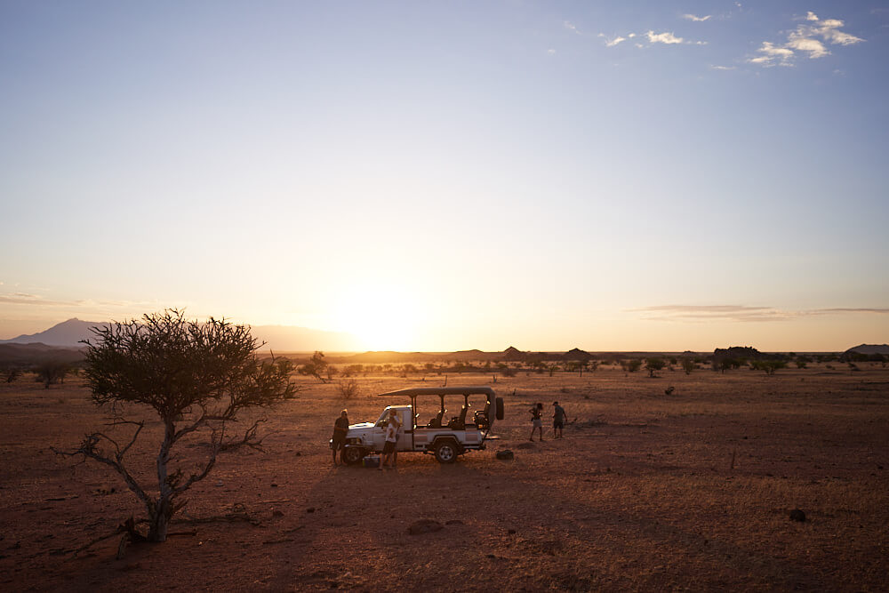 This picture shows a Land Cruiser with a group of people in a beautiful evening atmosphere. The surroundings are spacious.